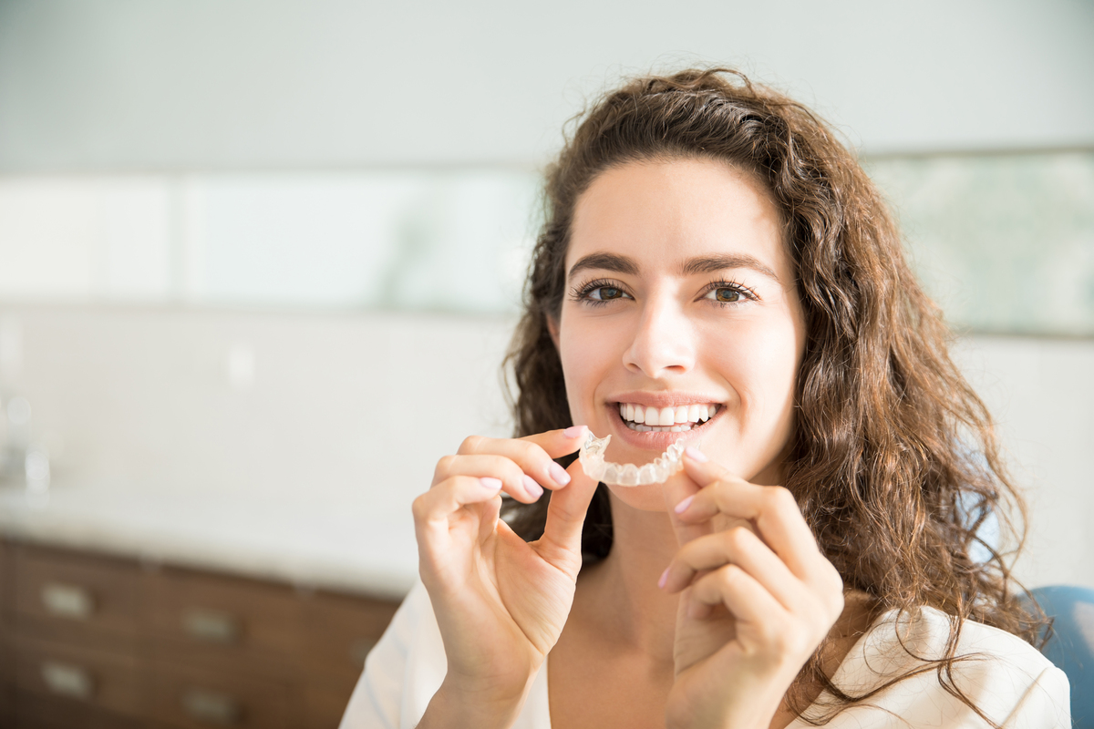 A woman holds a clear dental aligner in front of her mouth