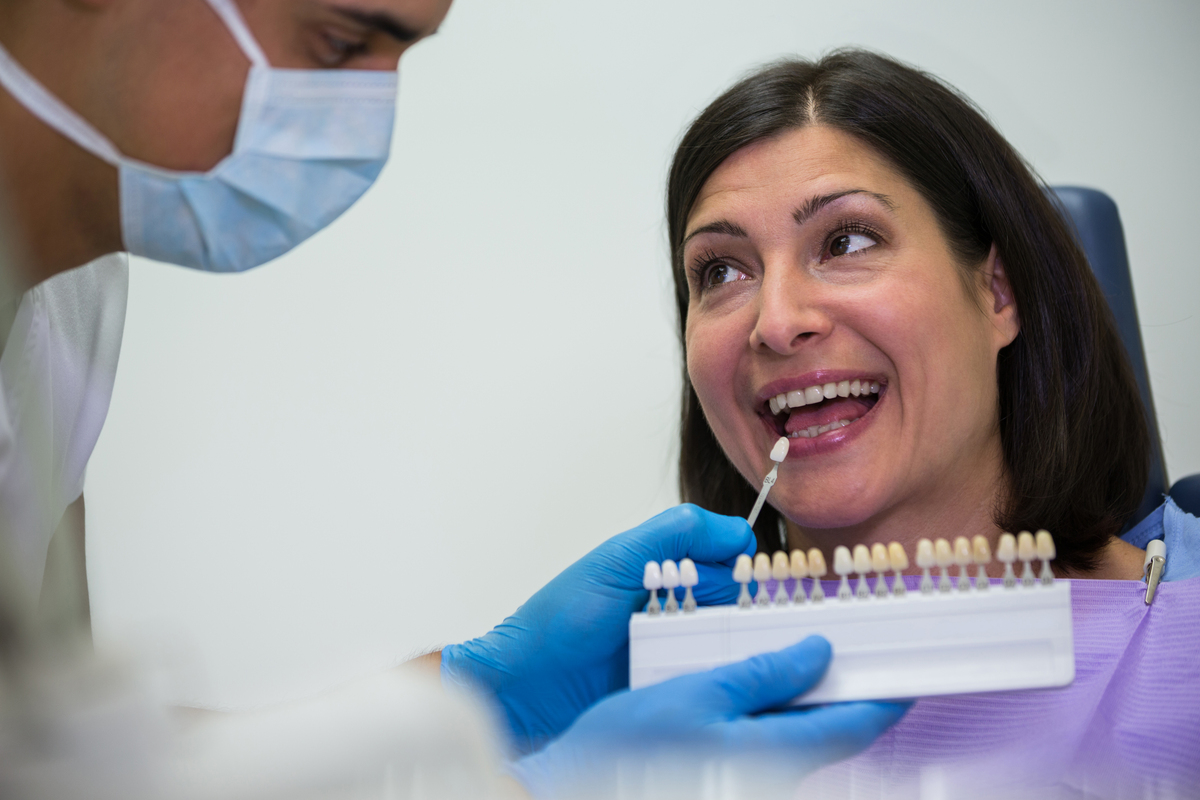 A dentist holds a sample dental implant to a patients mouth to match color