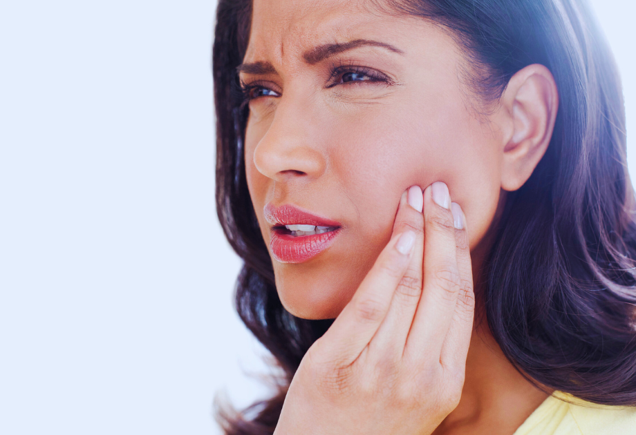 a woman winces and presses her fingers to her jaw