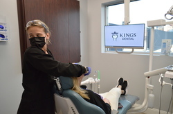 Person being examined in dentist office chair while woman looks behind her